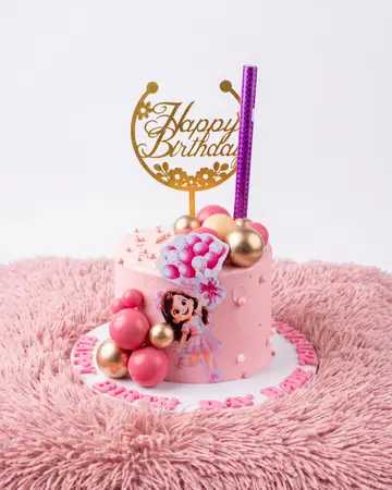 A bright pink birthday cake with a cartoon girl on the front, pink and gold spheres on top and a gold Happy Birthday topper.