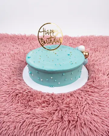 A smooth teal cake scattered with fine confetti and a single gold hoop topper.
